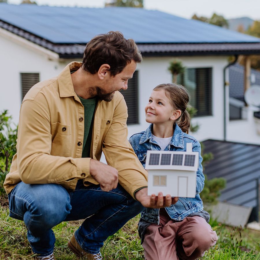 Vater mit seiner Tochter mit einem Modellhaus welches eine PV-Anlage zeigt